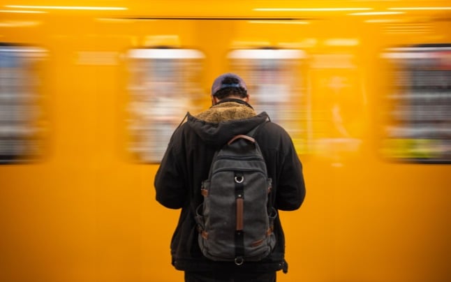 A man stands on the platform of a subway station in Berlin while a train passes him. 