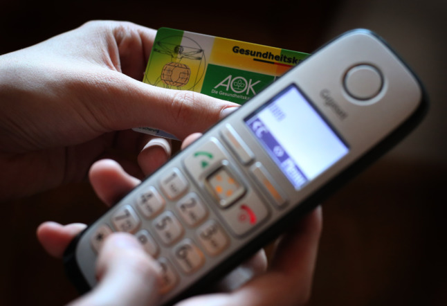 A person holds a German Krankenkasse card while making a phone call. 