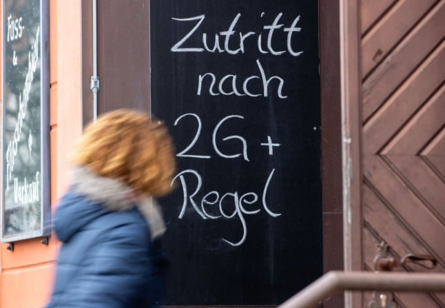 A woman walks past a 2G-plus sign at a restaurant in Griefswald.